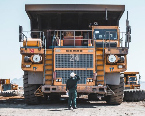 man in brown jacket standing beside yellow truck